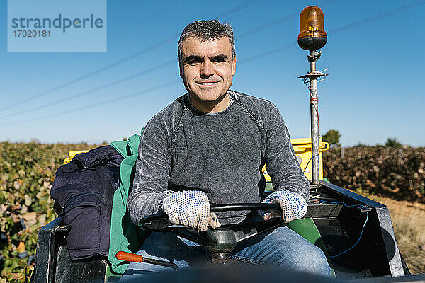 Lächelnder Mann fährt Traktor bei der Weinlese an einem sonnigen Tag