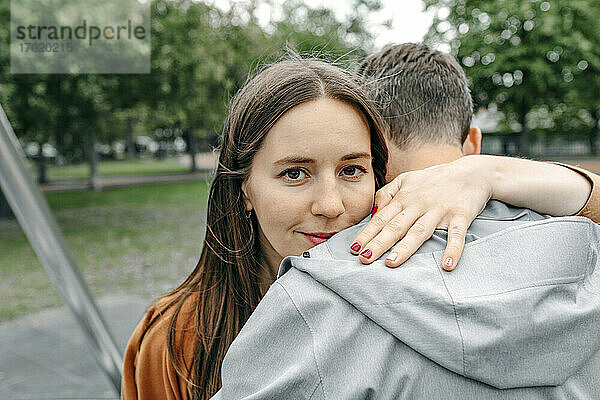 Lächelnde Freundin umarmt ihren Freund in einem öffentlichen Park