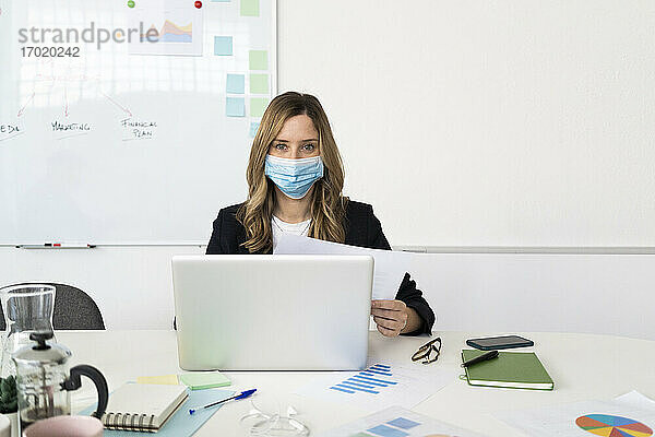 Frau mit Schutzmaske benutzt Laptop im Büro