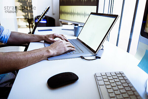 Berufstätiger  der einen Laptop benutzt  während er am Schreibtisch im Studio sitzt