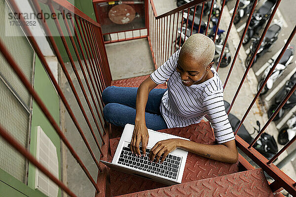 Kurzhaarige Frau sitzt auf einer Außentreppe und benutzt einen Laptop