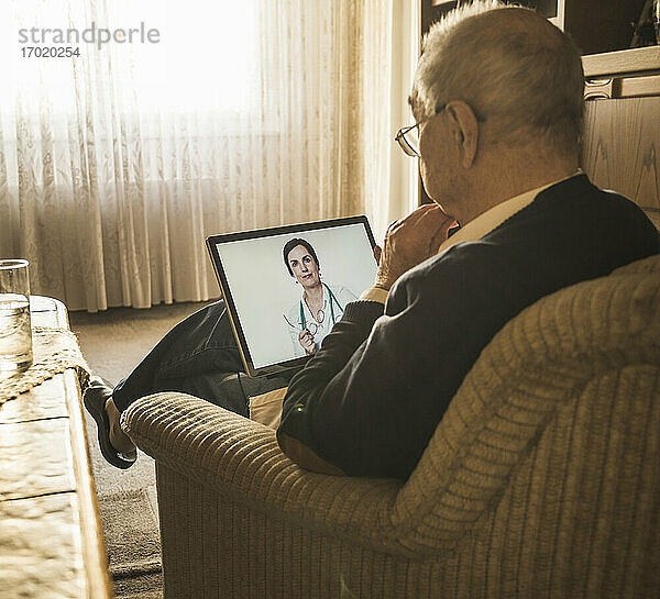 Älterer männlicher Patient  der über ein digitales Tablet online von einer Ärztin beraten wird