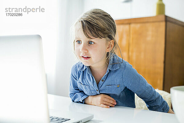 Mädchen schaut auf den Laptop  während sie zu Hause sitzt