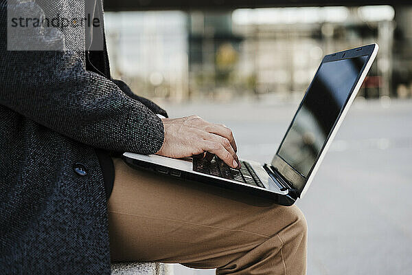Geschäftsmann  der im Freien sitzend am Laptop arbeitet