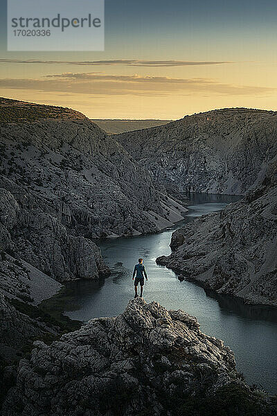 Mann steht auf Felsen und schaut auf den Fluss in einer Schlucht bei Sonnenuntergang