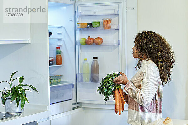 Junge Afro-Frau  die zu Hause ein Bündel Karotten in den Kühlschrank legt