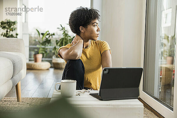 Frau mit digitalem Tablet  die durch das Fenster schaut  während sie zu Hause sitzt