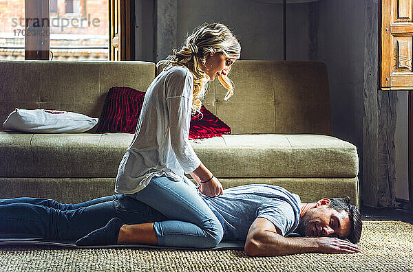 Junge Frau massiert ihren Freund auf dem Teppich im Wohnzimmer zu Hause