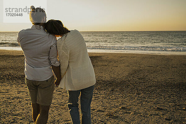 Romantisches Paar  das bei Sonnenuntergang am Strand spazieren geht