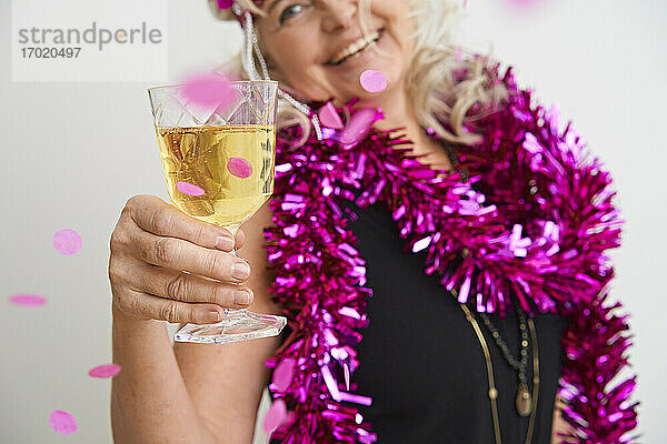 Glückliche ältere Frau hält ein Glas während einer Party vor weißem Hintergrund