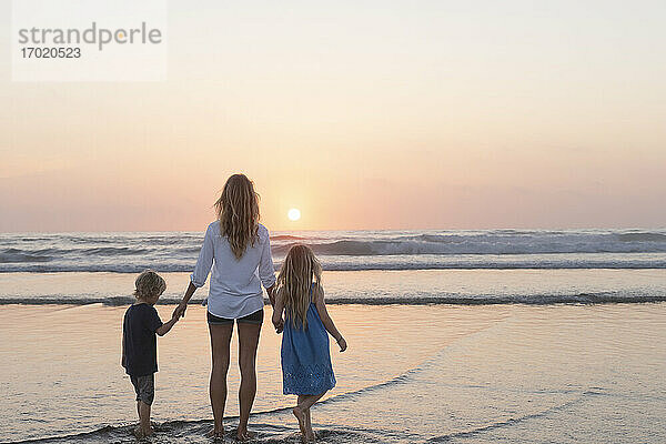 Mutter und Kinder betrachten den Sonnenuntergang  während sie am Strand stehen