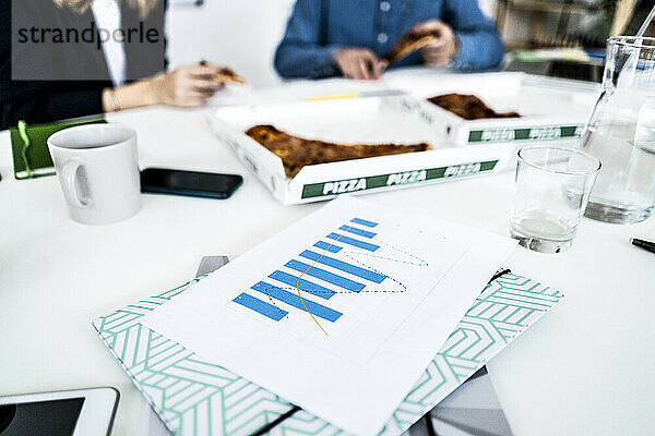 Geschäftsleute essen Pizza im Büro während der Pause  Dokumente im Vordergrund