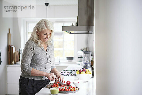 Frau im Ruhestand schneidet Erdbeeren auf einem Brett in der Küche zu Hause