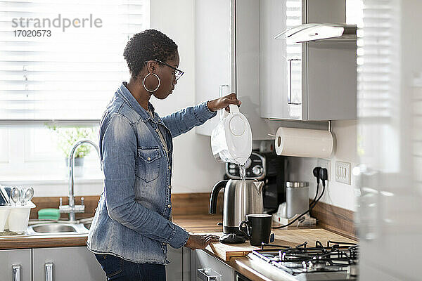 Frau gießt Wasser in einen Wasserkocher in der Küche
