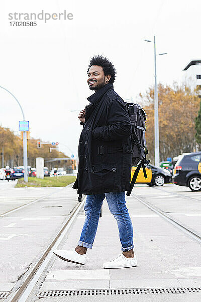 Hipster Mann mit Rucksack zu Fuß auf der Straße gegen klaren Himmel