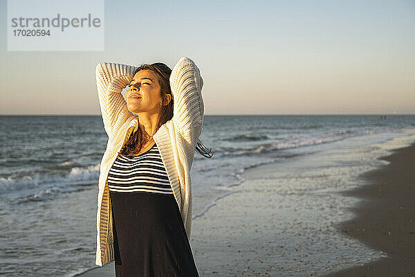 Lächelnde junge Frau am Strand gegen den klaren Himmel bei Sonnenuntergang