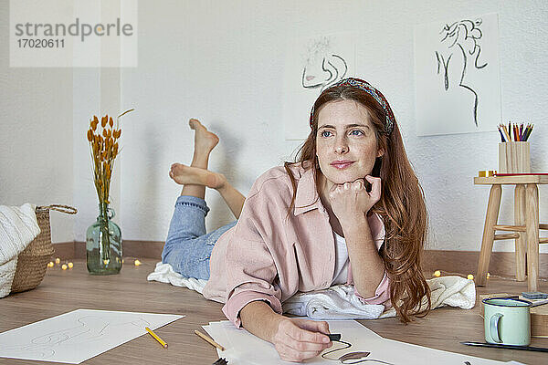 Weibliche Künstlerin mit Hand am Kinn träumt bei der Arbeit an einem Kunstwerk im Wohnzimmer