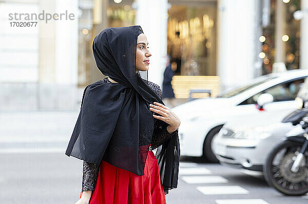 Porträt einer jungen schönen Frau mit schwarzem Hidschab  die mitten auf der Straße posiert