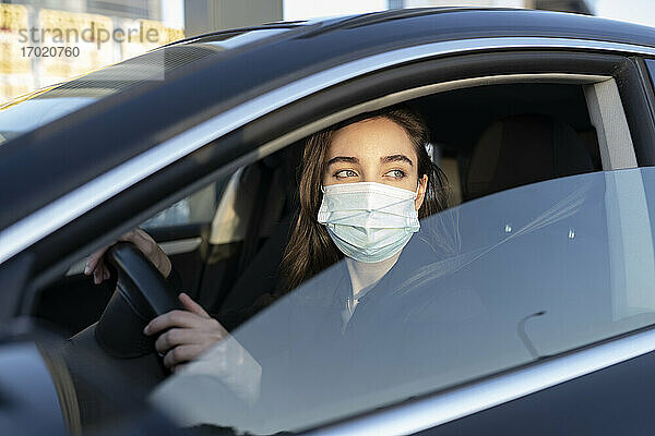 Geschäftsfrau mit Gesichtsschutzmaske  die beim Autofahren während der COVID-19 wegschaut