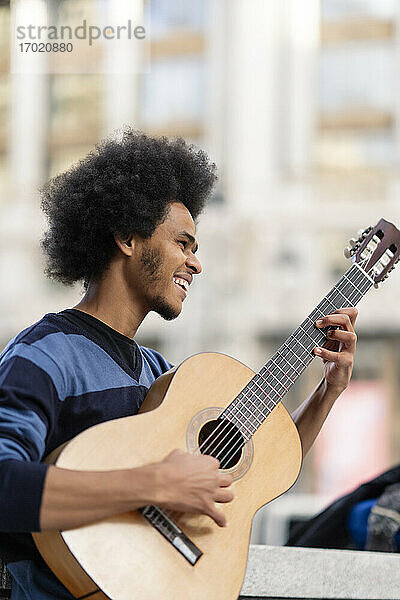 Junger Mann mit lockigem Haar  der im Freien stehend Gitarre spielt