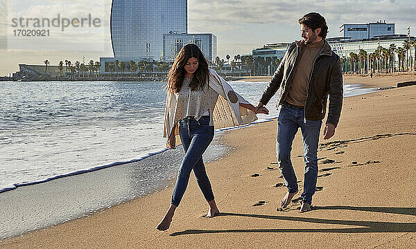 Junger Mann hält die Hand einer Frau beim Spaziergang am Strand