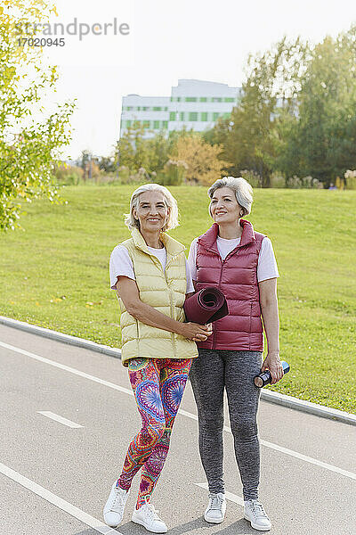 Lächelnde Freundinnen in Sportkleidung in einem öffentlichen Park an einem sonnigen Tag