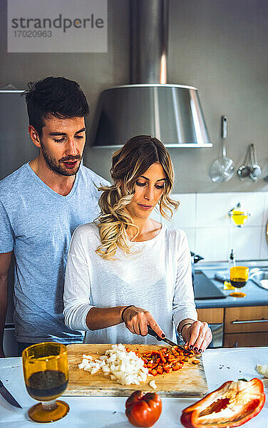 Junge Frau hackt Paprika  während sie Abendessen kocht und ein Mann zusieht