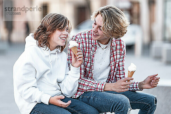 Lächelnder Junge isst Eis  während er neben einem Mann im Freien sitzt