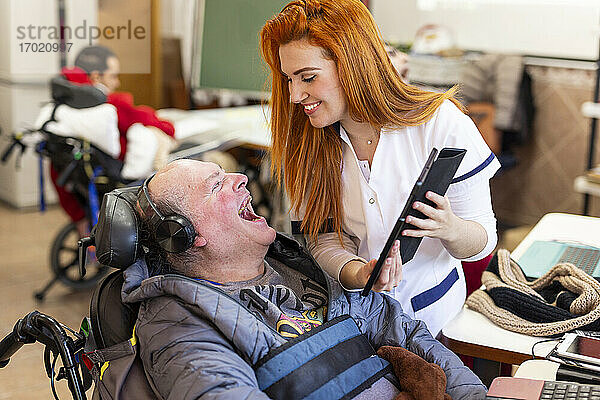 Eine lächelnde Krankenschwester zeigt einem glücklichen behinderten Mann im Pflegeheim ein digitales Tablet