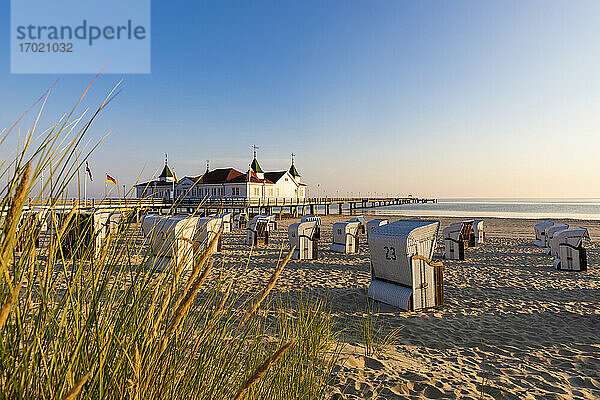 Deutschland  Mecklenburg-Vorpommern  Ahlbeck  Strandkörbe mit Kapuze am sandigen Küstenstrand mit Badehaus im Hintergrund