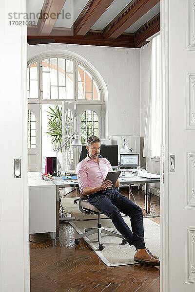 Älterer Geschäftsmann  der ein digitales Tablet benutzt  während er in einer Bürokabine sitzt
