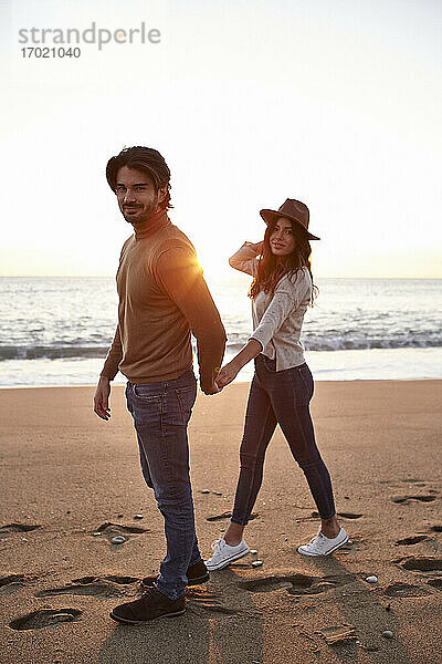 Junges Paar  das am Strand spazieren geht und sich an den Händen hält