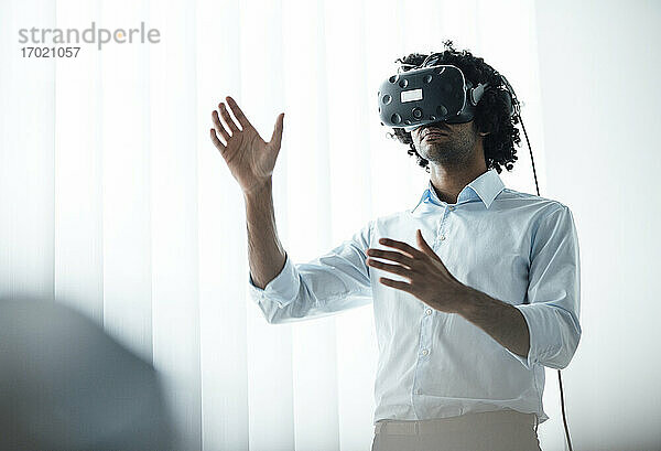 Junger Geschäftsmann trägt ein Virtual-Reality-Headset  während er im Sitzungssaal im Büro gestikuliert
