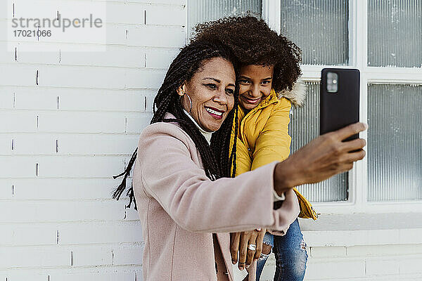 Lächelnde Mutter nimmt Selfie mit Tochter gegen die Wand