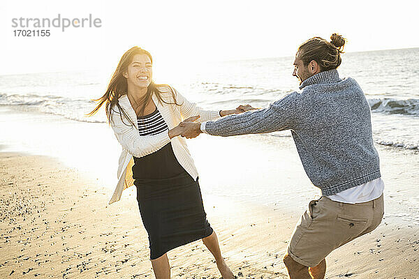 Fröhliches junges Paar hält sich an den Händen und genießt den sonnigen Tag am Strand