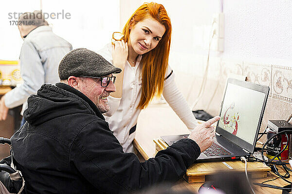 Lächelnder Mann  der von einer Betreuerin im Behindertenzentrum einen Laptop benutzt