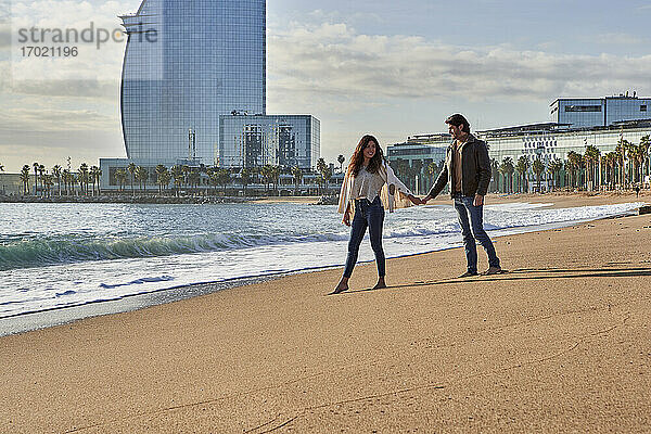 Junges Paar  das am Strand spazieren geht und sich an den Händen hält