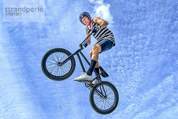 Unbekümmerter junger Mann  der mit dem Fahrrad gegen den blauen Himmel im Fahrradpark springt