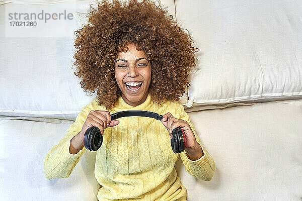 Lachende Frau  die nach der Arbeit im Schlafzimmer mit Kopfhörern spielt