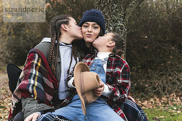 Zwei Mädchen küssen ihre Schwester in einer Herbstlandschaft