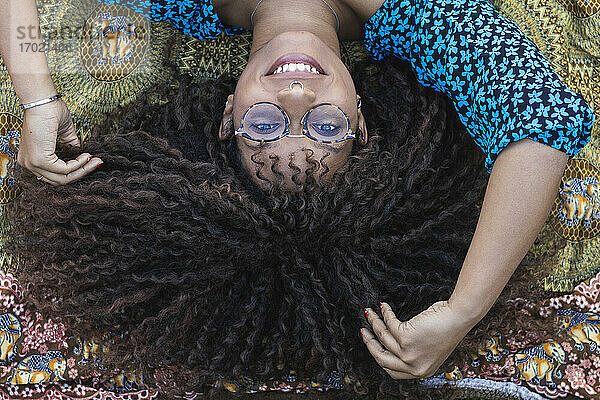 Lächelnde Afro-Frau mit Hand im Haar auf einer Decke im öffentlichen Park liegend
