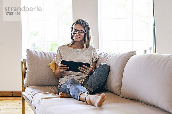 Entspannte brünette Geschäftsfrau  die auf dem Sofa sitzt und ein digitales Tablet im Wohnzimmer zu Hause benutzt
