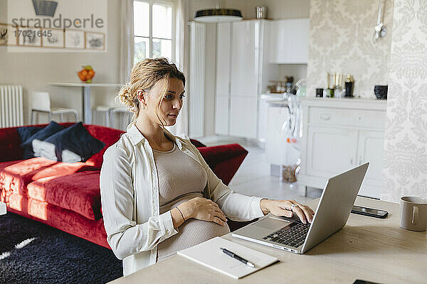 Schwangere Geschäftsfrau arbeitet am Laptop am Schreibtisch zu Hause
