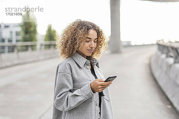 Schöne junge Afro-Frau  die ein Smartphone benutzt  während sie auf einer Brücke in der Stadt steht