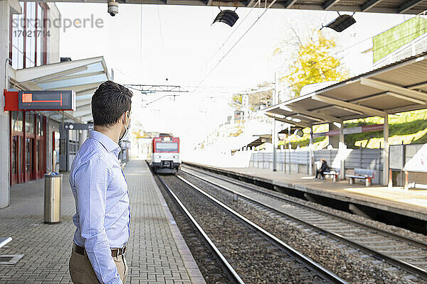 Geschäftsmann mit Gesichtsmaske wartet am Bahnsteig auf einen Zug