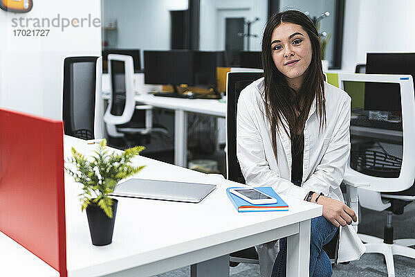 Lächelnde Geschäftsfrau mit Laptop und Smartphone auf dem Schreibtisch sitzend