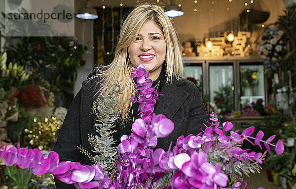 Porträt einer lächelnden Floristin  die einen Strauß lila Eukalyptusblätter in einem Blumenladen hält