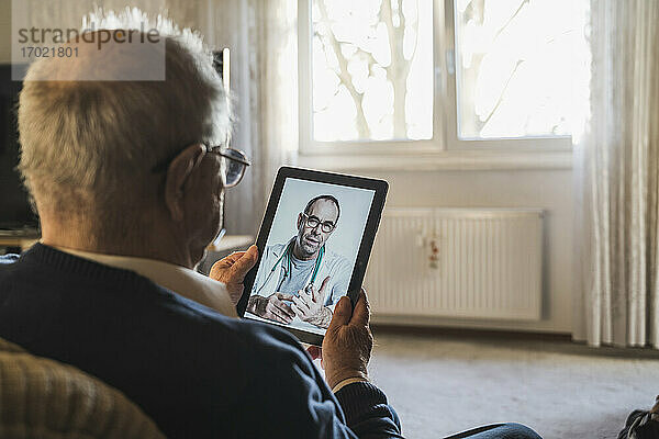 Älterer Mann lässt sich von einem männlichen Arzt per Videoanruf über ein digitales Tablet zu Hause beraten