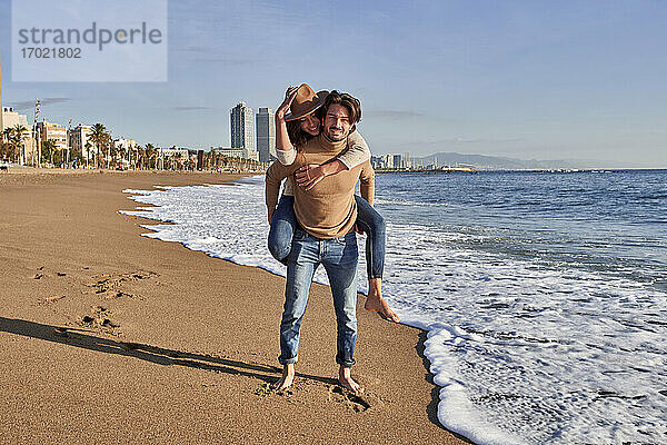Freund nimmt seine Freundin am Strand huckepack