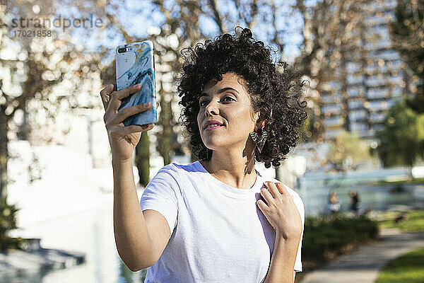 Lächelnde Frau  die ein Selfie mit ihrem Mobiltelefon macht  während sie im Freien steht